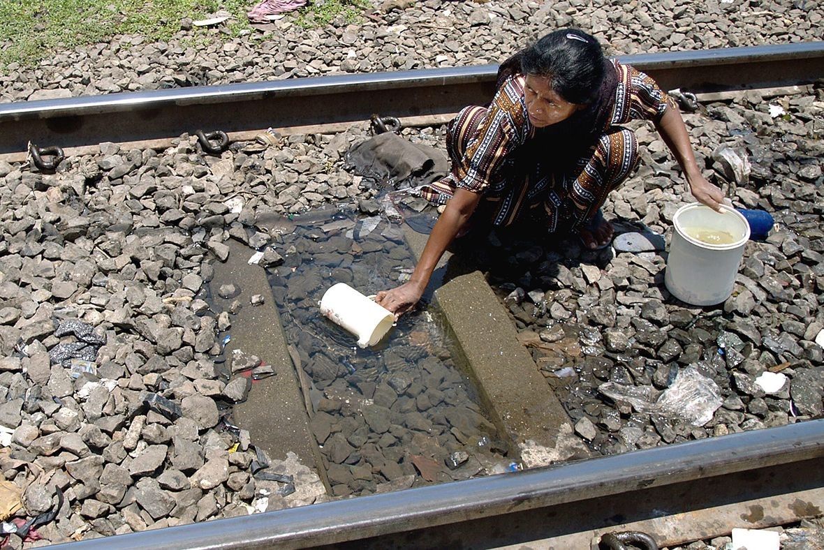 Người dân khu ổ chuột lấy nước uống từ vũng nước giữa đường ray tàu hỏa tại Mumbai - Ảnh: Reuters